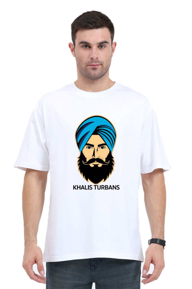 A man wearing a white oversized t-shirt with a graphic print of a person wearing a blue turban and the text 'KHALIS TURBANS'.