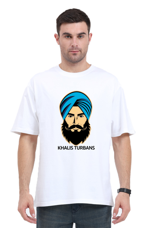 A man wearing a white oversized t-shirt with a graphic print of a person wearing a blue turban and the text 'KHALIS TURBANS'.